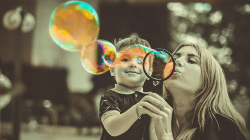 child blowing bubbles with mom