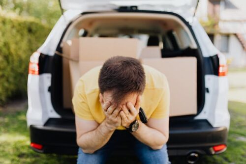 man with head in hands and boxes in trunk of car